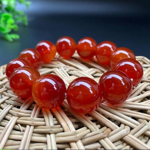 Rotes Edelsteinarmband auf rundem Holzuntersetzer mit geflochtenem Muster.