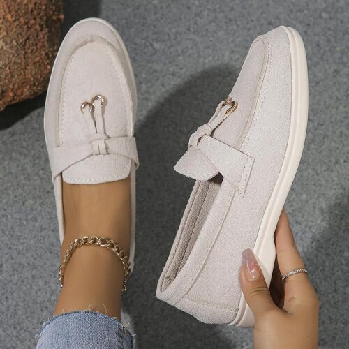 Beige Loafers mit Schnalle auf grauem Boden und einer Hand im Bild. Beige Loafers mit Schnalle auf grauem Boden und einer Hand im Bild.