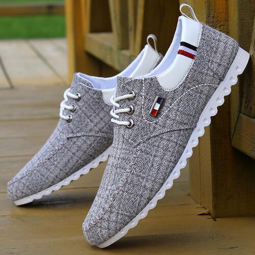Graue Sneaker aus Stoffmaterial mit weißen Schnürsenkeln auf Holzboden.