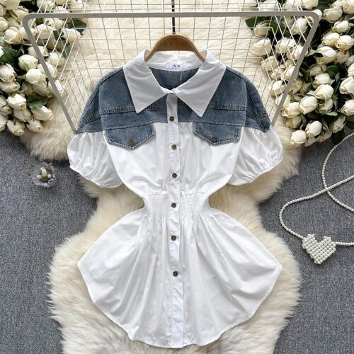 Weiße Hemdbluse mit Denim-Details liegt auf Teppich, umgeben von Blumen.