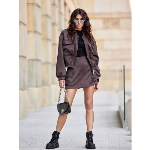 Frau in brauner Jacke und Rock mit Sonnenbrille, schwarzer Tasche und Stiefeln.