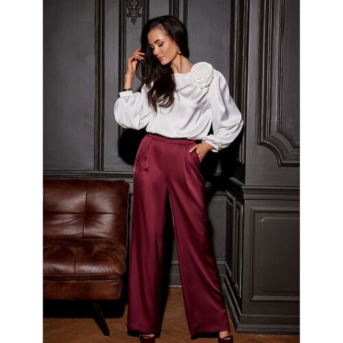 Frau in weißer Bluse und roten Hosen steht in elegantem Raum.