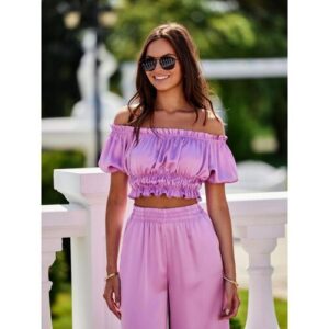 Person in rosa Off-Shoulder-Outfit mit Sonnenbrille steht auf einer Terrasse.