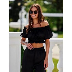 Person trägt schwarzes, schulterfreies Outfit, steht draußen in sonniger Umgebung.