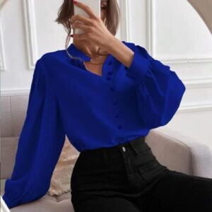 Person in blauer Bluse vor Spiegel in elegantem Innenraum mit Couch.