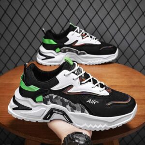 Schwarze und weiße Sneaker mit grünen Details auf Holztisch, Mauer im Hintergrund.