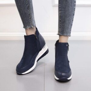 Blaue Sneakerstiefel mit weißen Sohlen, getragen mit Jeans auf grauem Boden.