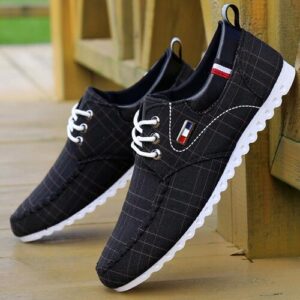 Schwarze Sneaker mit weißer Sohle, auf Holzboden gestützt.