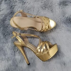 Goldene Stiletto-Plateauschuhe auf grauem, pelzigem Untergrund.