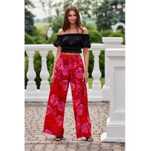 Person trägt schwarzes Off-Shoulder-Top und rote Hose mit Blumenmuster, steht draußen.