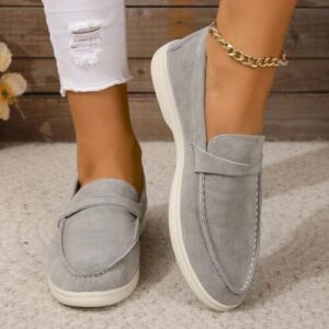 Graue Slipper auf beigem Teppich mit weißer zerrissener Jeans und goldener Fußkette.