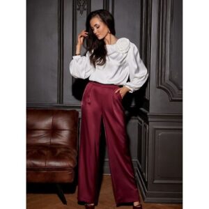 Frau in weißer Bluse und roten Hosen steht in elegantem Raum.