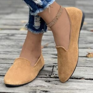 Braune Loafers auf Holzplanken mit zerrissenen Jeans im Hintergrund.