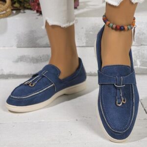 Blaue Leinenschuhe mit weißer Sohle auf grauem Boden, Fußkettchen am Knöchel.