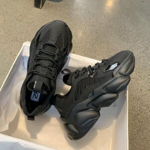 Schwarze Sneaker in einem offenen Schuhkarton auf einem Betonboden.