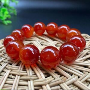 Rotes Edelsteinarmband auf rundem Holzuntersetzer mit geflochtenem Muster.