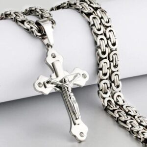 Kreuzanhänger aus Metall mit großer Kette auf einer hellen Oberfläche.