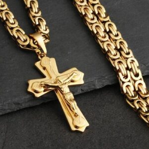 Goldene Kette mit Kreuzanhänger auf grauer Steinoberfläche.