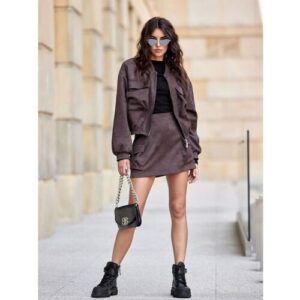 Frau in brauner Jacke und Rock mit Sonnenbrille, schwarzer Tasche und Stiefeln.