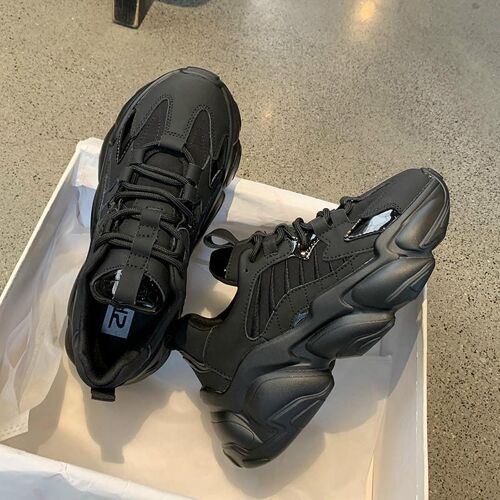 Schwarze Sneaker in einem offenen Schuhkarton auf einem Betonboden.