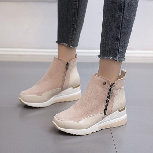 Hellbraune Stiefeletten mit Reißverschluss, getragen zu dunklen Jeans auf grauem Boden.