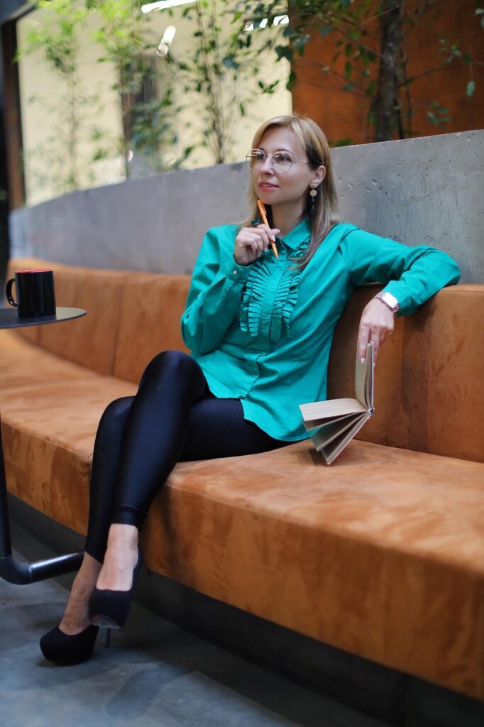 Person sitzt auf einem Sofa, hält Buch, mit Kaffeetasse und Pflanzen im Hintergrund.