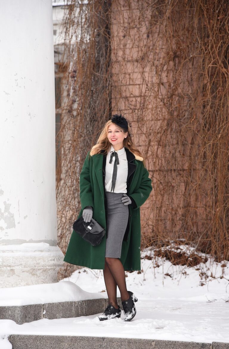 Frau in Wintermode mit grünem Mantel vor einer schneebedeckten Landschaft mit Säule.